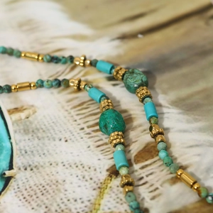 Bohemian turquoise bead necklace with green raw stone and gold metal accents on vintage fabric