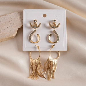 Detail showing golden geometric earrings with crystals and tassels on beige silk background