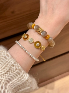 Détail macro de bracelets superposés plaqués or 18k avec zircons et breloques acétate