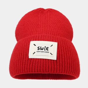 Detail of red knit beanie featuring a white square woven label with letter stitching