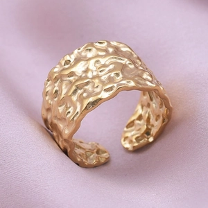 Macro shot of gold wide band ring with irregular lava texture on pink velvet