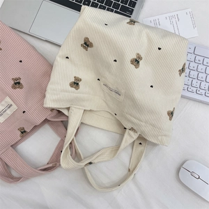 Detail shot of corduroy tote bags with bear print and canvas studio label on desk