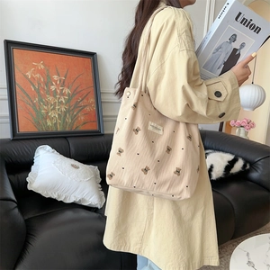 Detail of corduroy tote bag with embroidered bear pattern worn over the shoulder