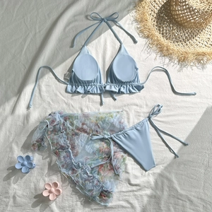 Flat lay of light blue ruffle bikini with colorful floral mesh sarong and beach accessories
