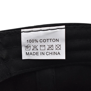Close-up of white 100% cotton wash care label on a black baseball cap fabric