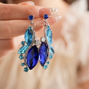 Close-up of vintage rhodium rhombus earrings with blue crystals held by hand