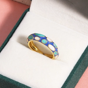Détail d'une bague en émail bleu et vert avec bords dorés dans un écrin à bijoux en velours