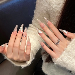 Dettaglio macro di unghie finte a stiletto con rilievo a farfalla bianca e perle lucide