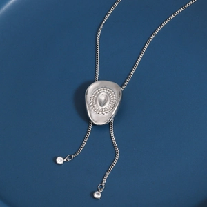 Macro detail of silver cowboy hat pendant with gemstone and adjustable metal tassels