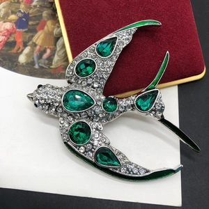 Broche hirondelle raffinée en métal argenté avec cristaux émeraude et strass scintillants