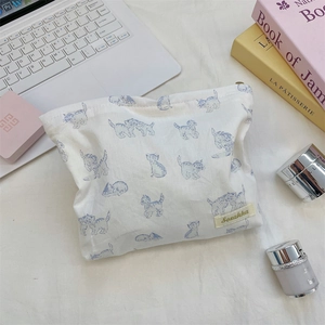 Flat lay of cream toiletry bag with blue cat prints and skincare props on a desktop