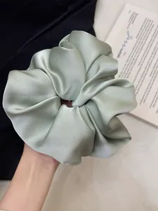 Detailed close-up of a large sage green satin oversized scrunchie with silky texture