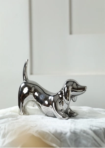 Close-up of a silver mirror-finish dachshund dog statue on white fabric