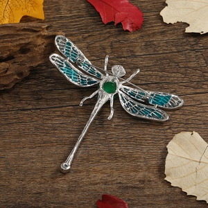 Vintage dragonfly brooch in silver metal with green faux gems on autumn wood background