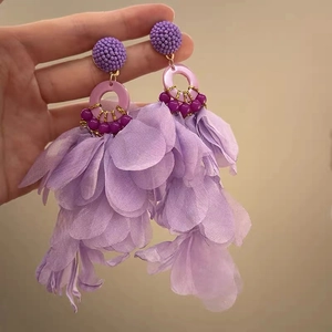 Handheld close-up showing purple fabric flower petals and bead tassels on long earrings
