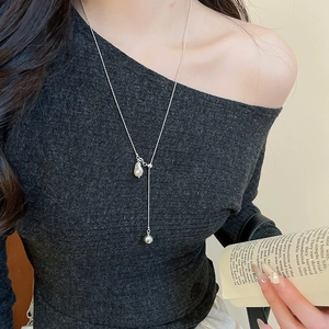 Close-up of a silver Y-shaped necklace with a pearl bead and metal ball on a model