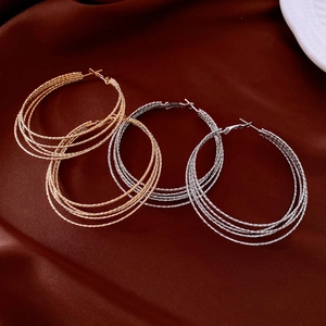 Detailed view of layered gold and silver hoop earrings on a dark silk fabric background