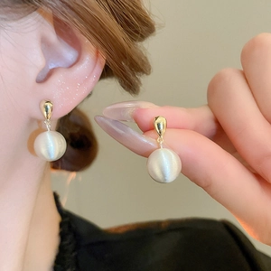 Gros plan d'une boucle d'oreille dorée avec texture de sphère blanche brossée