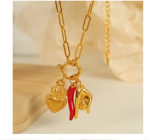 Detail of gold paperclip necklace with crown heart, red chili, and horn hand charms
