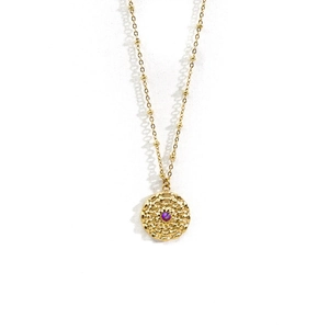 Close-up of golden disk pendant with textured surface and purple gemstone center