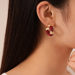 Détail de boucles d'oreilles créoles dorées en C avec cordon en cuir rouge foncé