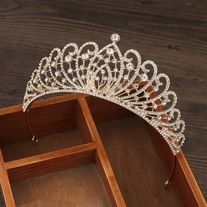 Golden alloy crown with white rhinestones and heart motif on a dark wooden box