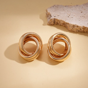 Detail of gold geometric multi-loop twisted knot earrings on a textured stone surface