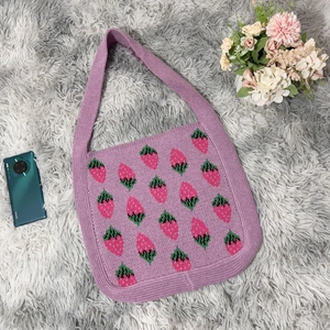 Detailed knit texture of purple strawberry tote bag on grey faux fur background