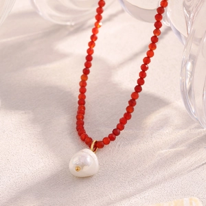 Macro detail of red beaded necklace with baroque pearl pendant and 18K gold plated clasp