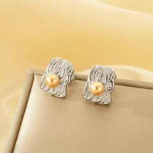 Detail of irregular textured silver square stud earrings with central gold pearls