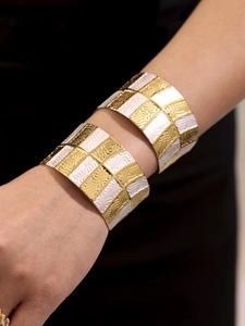Dettaglio di bracciali a polsino larghi con motivi a scacchi oro e bianco e trama ondulata