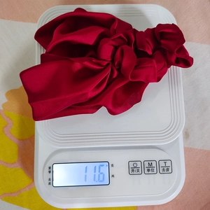 Detail showing red satin scrunchie with bow knot weighing 11.6g on a digital scale