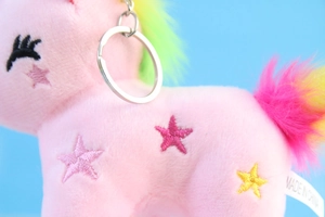 Dettaglio dell'unicorno di peluche rosa con anello in metallo e stelle ricamate