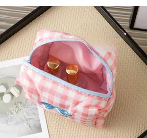 Close-up of pink plaid makeup bag with a blue bow and zipper on a woven mat
