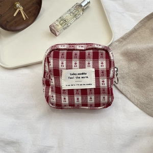 Detail of red checkered fabric pouch with metal ring zipper on textured background