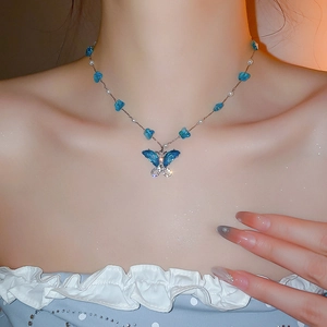 Detalle de collar de mariposa con pedrería azul y perlas lucido por una modelo real