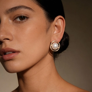 Close-up of pearl and gold alloy stud earring with irregular hoop on model's ear