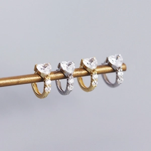 Macro shot of gold and silver heart-shaped zircon hoop earrings on a metal bar