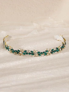 Close-up of green and clear crystals on a gold leaf bridal sash with white ribbons