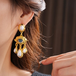 Macro detail of vintage gold eye earrings with dangling teardrop pearls on model