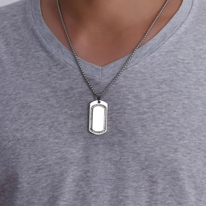Close-up of a silver rectangular military dog tag pendant with small rhinestones on a male model
