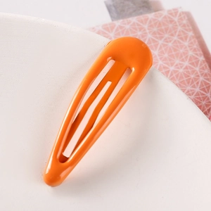 Close-up of a glossy orange teardrop metal hair clip on a minimalist white plate