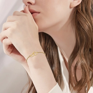 Detail of a minimalist gold double-heart linked chain bracelet on a female wrist