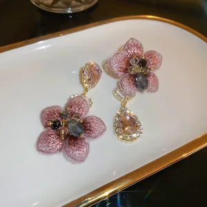 Macro detail of asymmetric pink embroidered floral earrings with crystal and gemstone drops