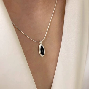 Close-up of minimalist silver snake chain necklace with an oval black onyx gemstone pendant