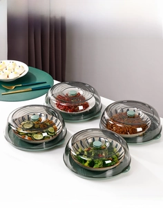 Close-up of four transparent food covers with grey-green handles on white tabletop