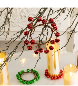 Detail of festive red and green metal bell wreaths hanging on rustic branches with warm candle light