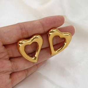 Elegant gold hollow heart earrings in titanium steel held by hand against white fabric