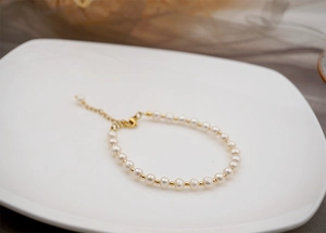 Detail of freshwater pearl bracelet with gold beads on a white ceramic tray