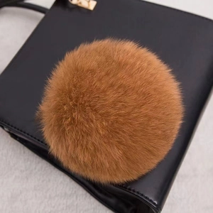 Gros plan d'un pompon en fourrure marron dense sur la surface d'un sac à main en cuir noir